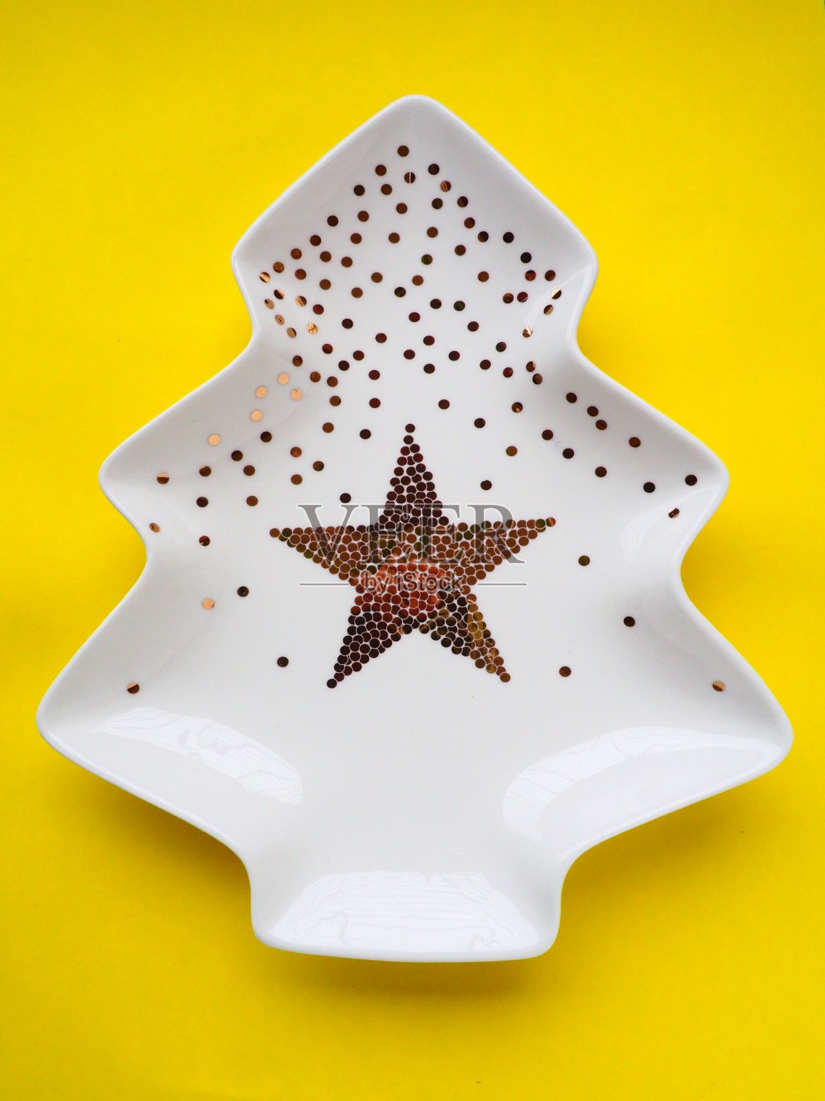 圣诞树形状的白色盘子，上面有金色的装饰，中间有一颗星星。黄色背景。新年或圣诞卡片。广告背景和祝贺。副本的空间。照片摄影图片