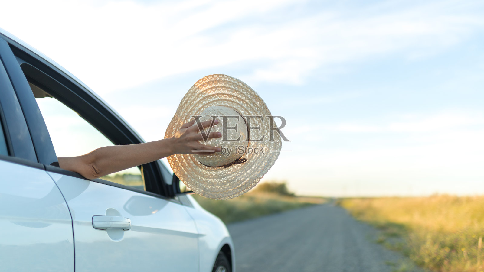 一个女孩从一辆汽车的窗户里伸出手拿出一顶帽子。自由和冒险的概念。照片摄影图片