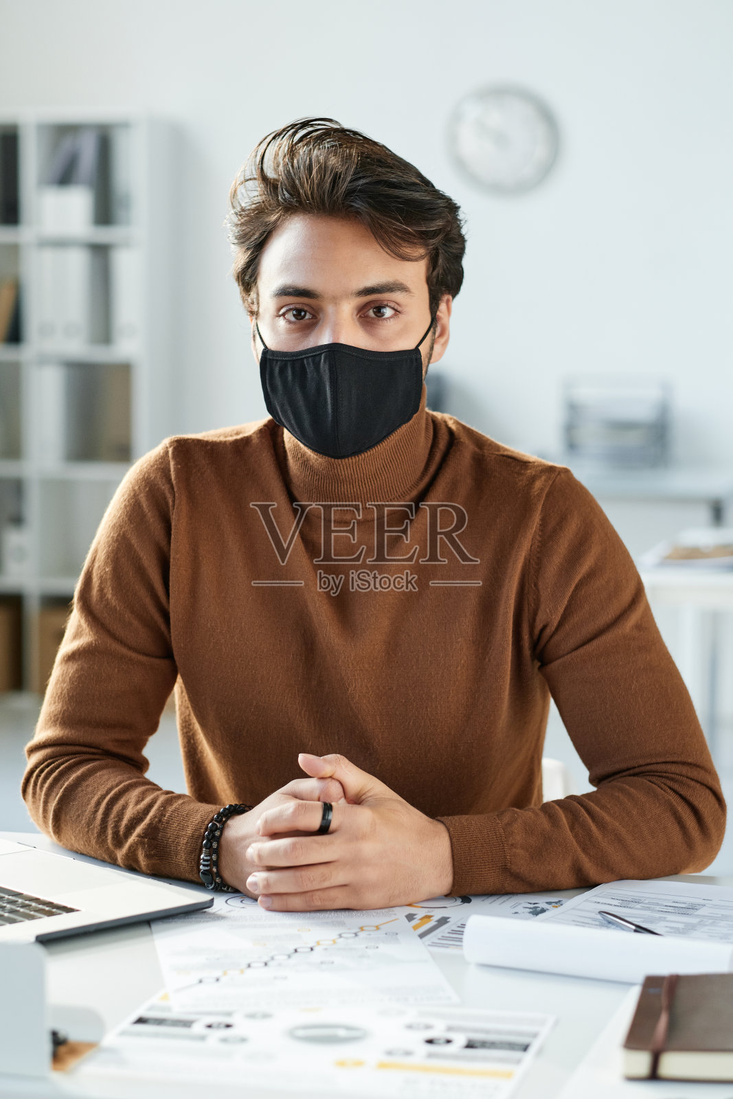 画像的年轻中东男子在黑色面具坐在桌旁与文件和工作报告照片摄影图片