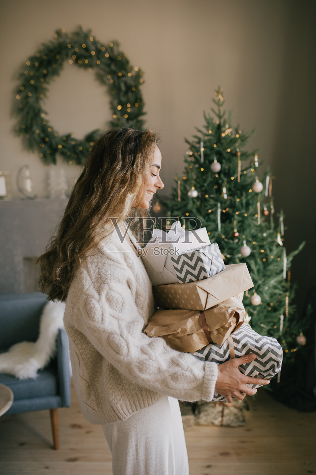 年轻漂亮的女人拿着礼品盒和礼物在一个温馨的房间里，背景是圣诞树。假期准备。照片摄影图片