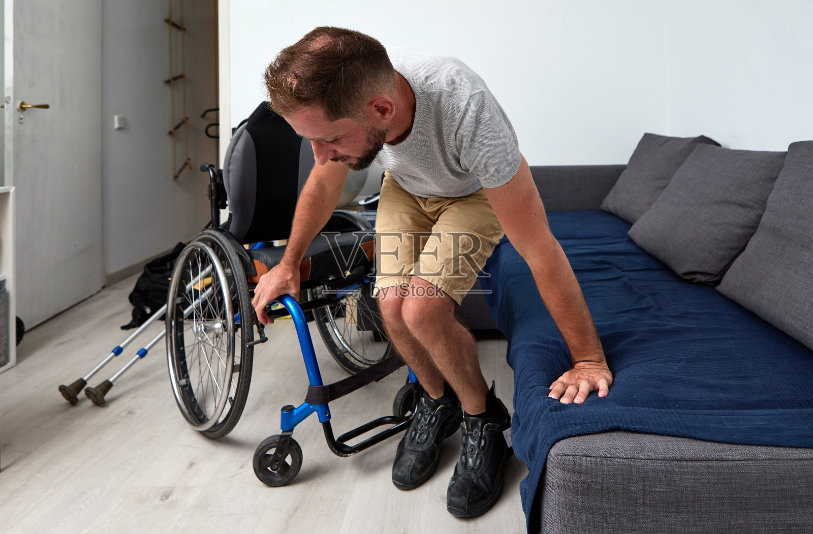 一个年轻人试图用他手臂的力量从轮椅上坐在沙发上照片摄影图片