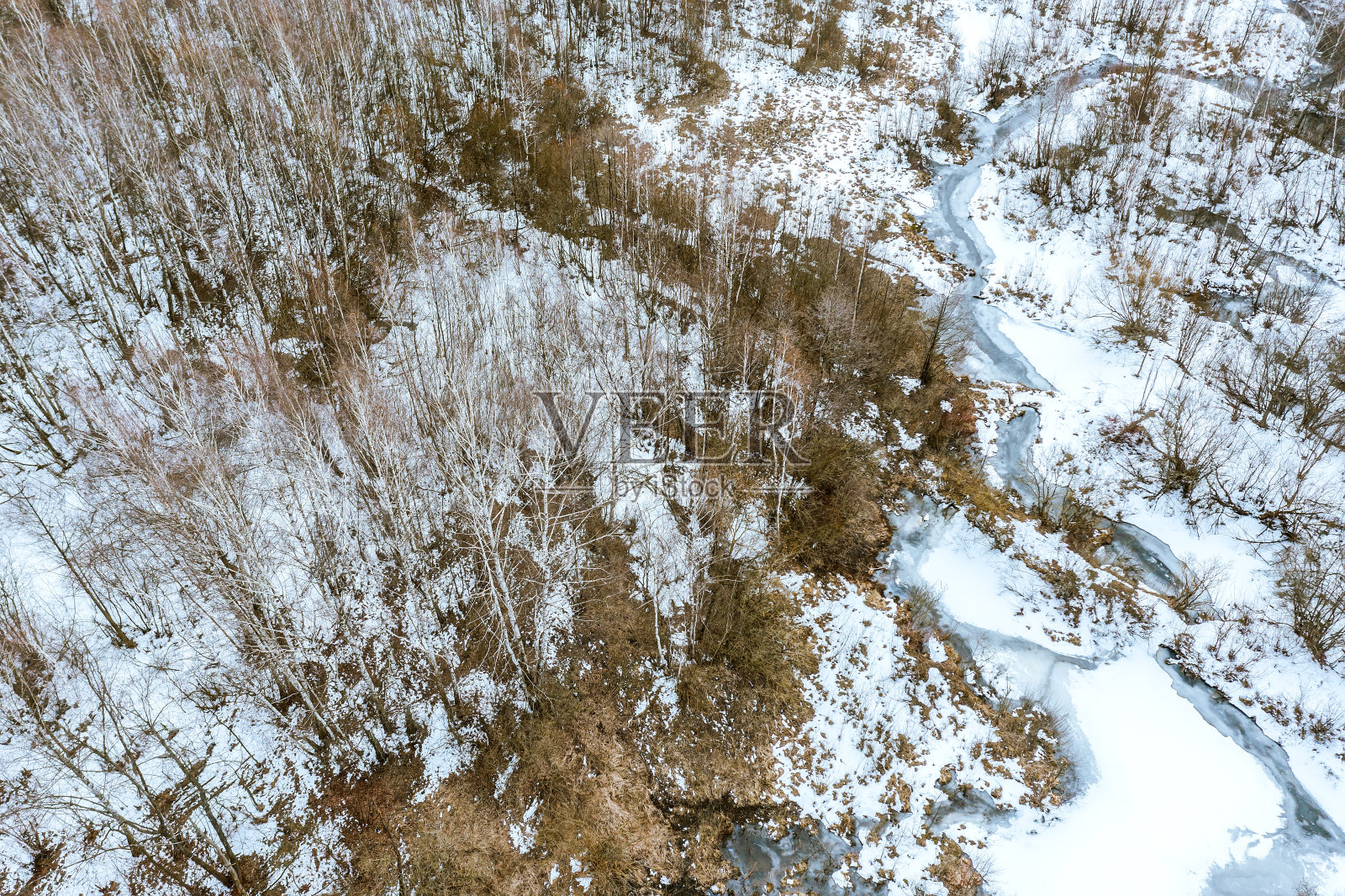 冬天的风景。冰雪覆盖的冬季森林中蜿蜒的小河流。鸟瞰图。照片摄影图片