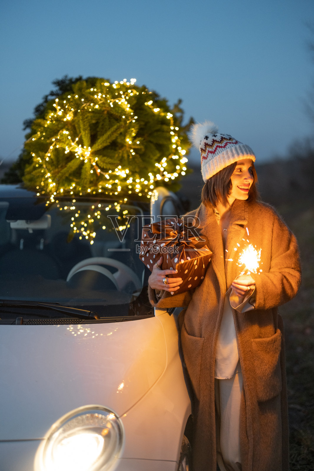 在屋外的圣诞树和汽车附近用洒水器的女人照片摄影图片