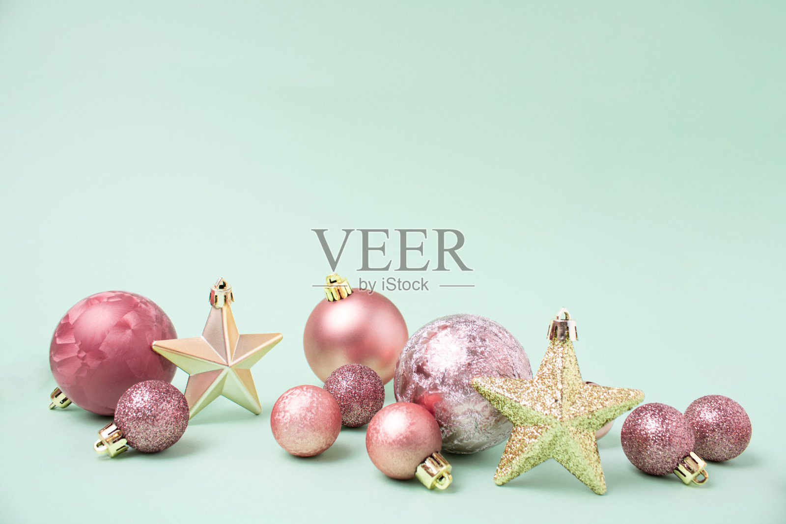 淡雅的粉红色小玩意和闪亮的金色星星作为圣诞装饰在淡雅的绿色背景。最小的新年复制空间。照片摄影图片