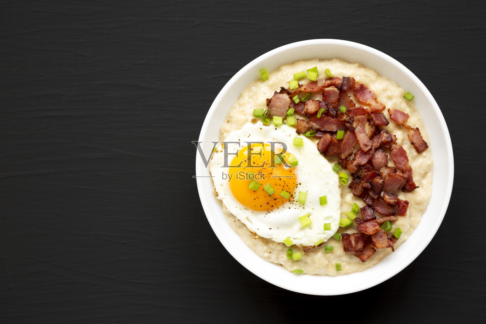 自制奶酪培根咸味燕麦碗在黑色背景上，俯视图。在头顶上，从上面，平放。副本的空间。照片摄影图片