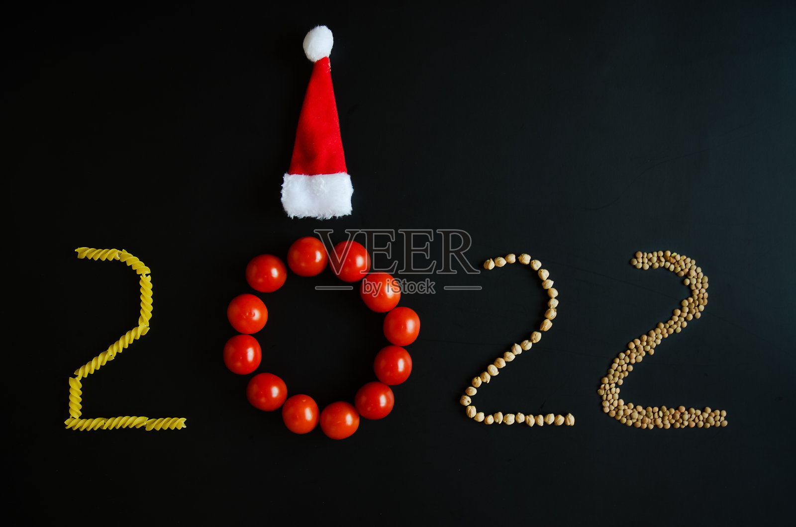 2022年新年数字。新年快乐的象征。假期创意概念。健康的素食。新鲜的红番茄，意大利面，圣诞帽在黑色的背景。圣诞贺卡。副本的空间。照片摄影图片