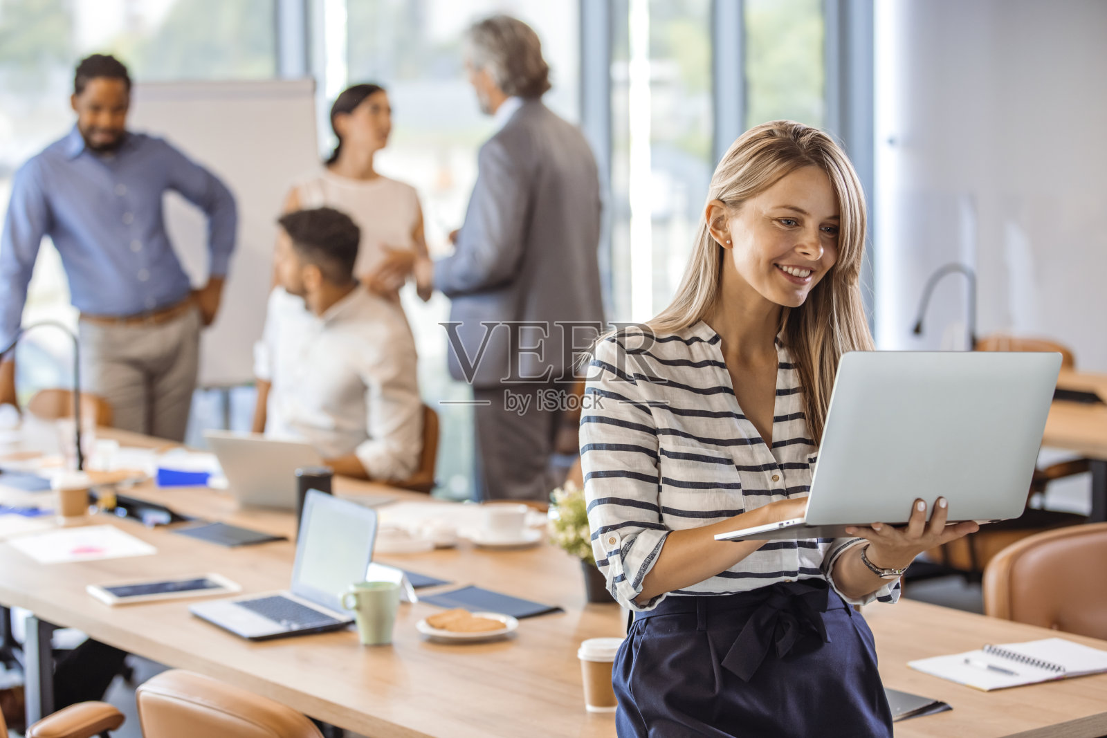 女经理手持笔记本电脑站在现代化的办公室里。照片摄影图片