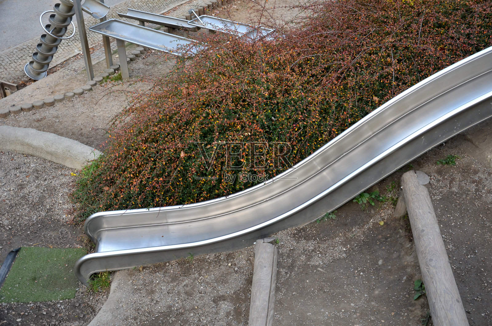 操场上的不锈钢滑梯配有混凝土山丘、岩石和木制栅栏。大型光滑管滑动儿童与冲击格子橡胶垫。管子是一个开槽照片摄影图片