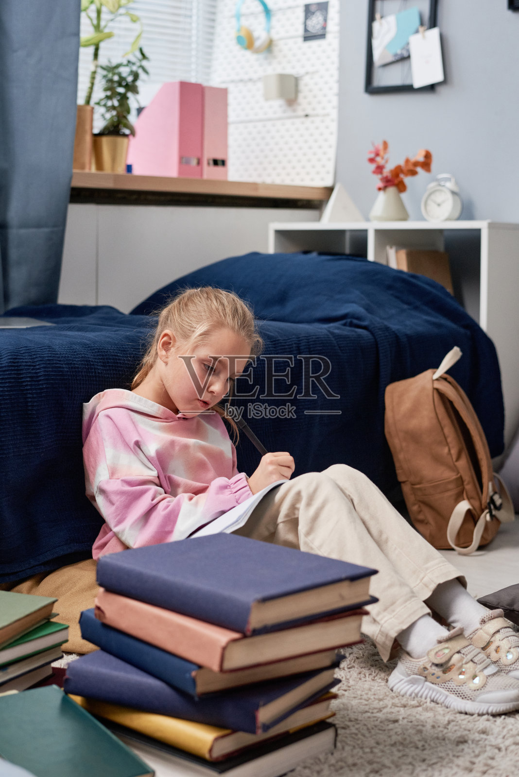 一个穿着连帽衫的女生坐在地板上，在一堆书后面，专心致志地准备考试照片摄影图片