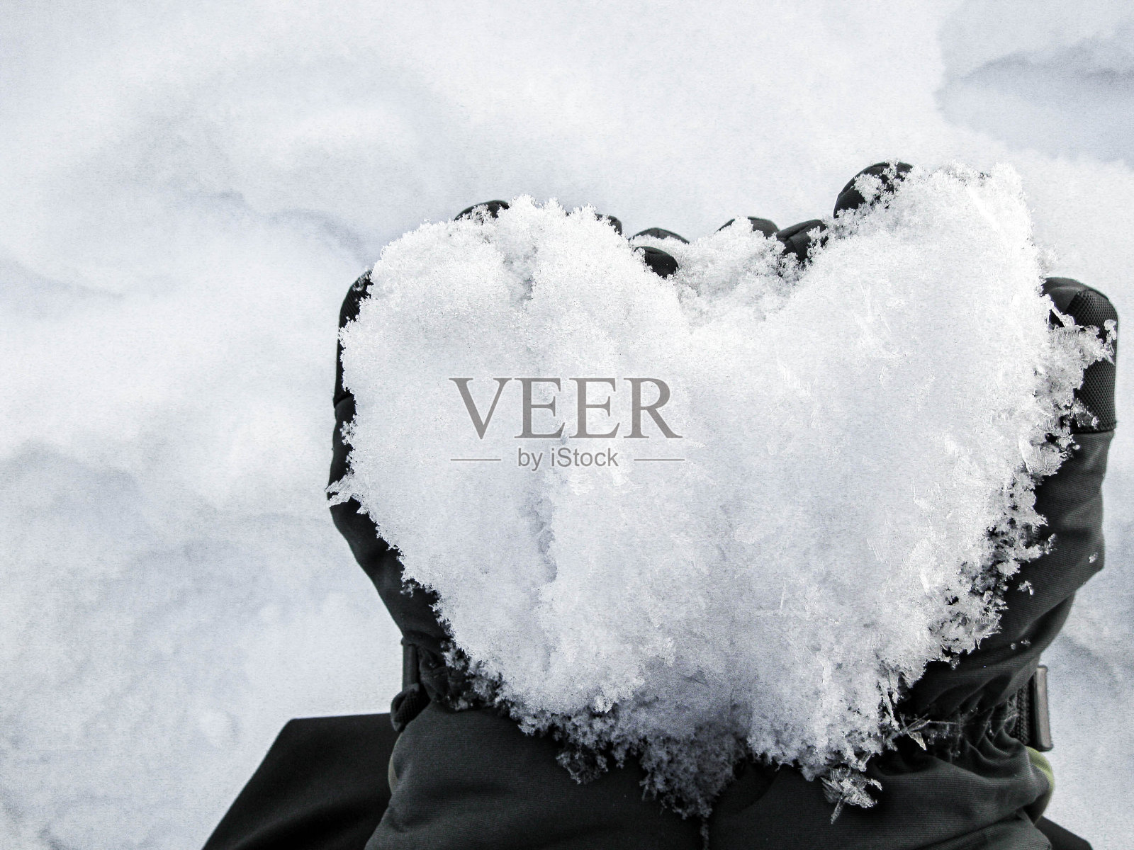 在白雪的背景下，手拿着一个心形的雪球照片摄影图片