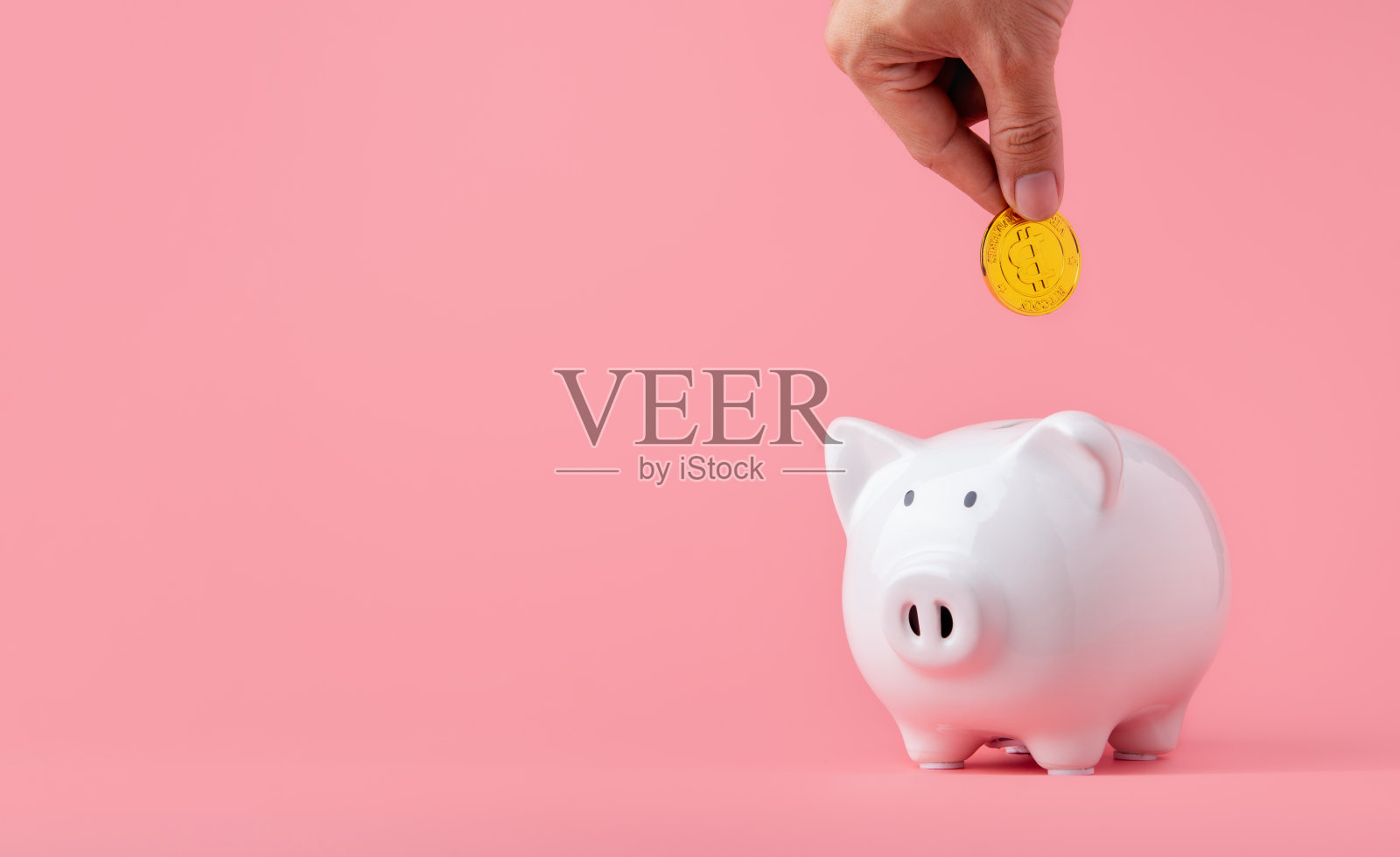 省钱和投资理念。手把比特币到储蓄罐在粉红色的背景和复制空间照片摄影图片