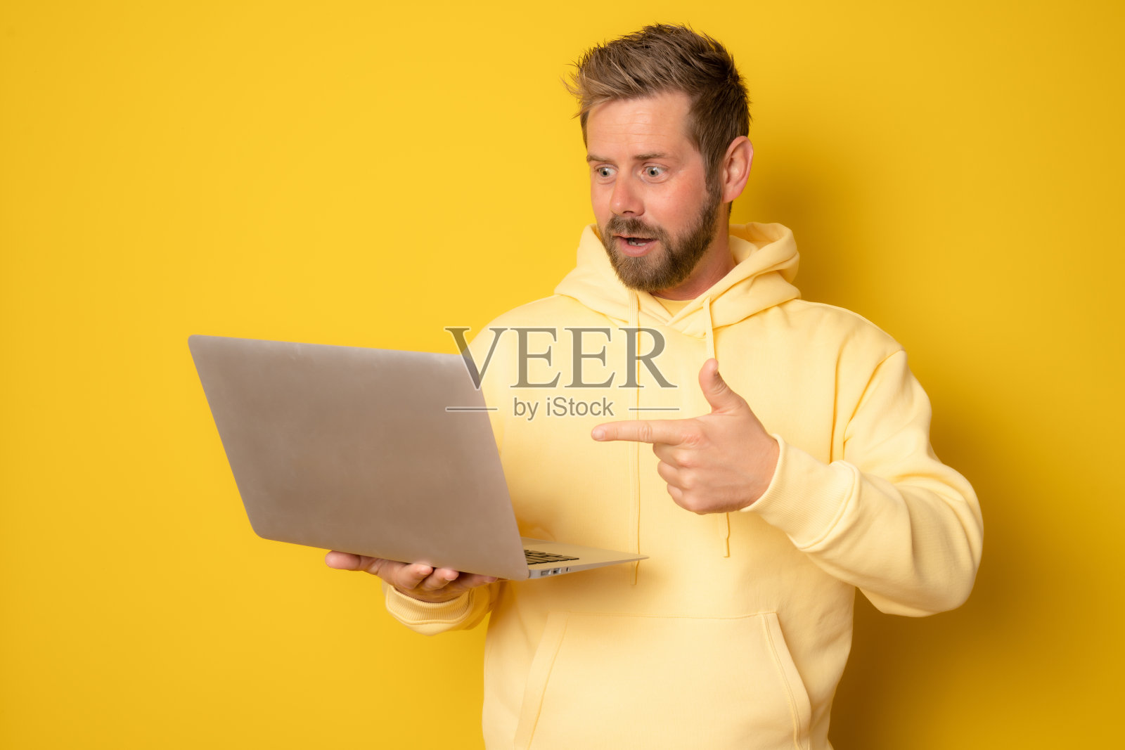 一个兴奋的年轻人的肖像，拿着笔记本电脑孤立的黄色背景。照片摄影图片