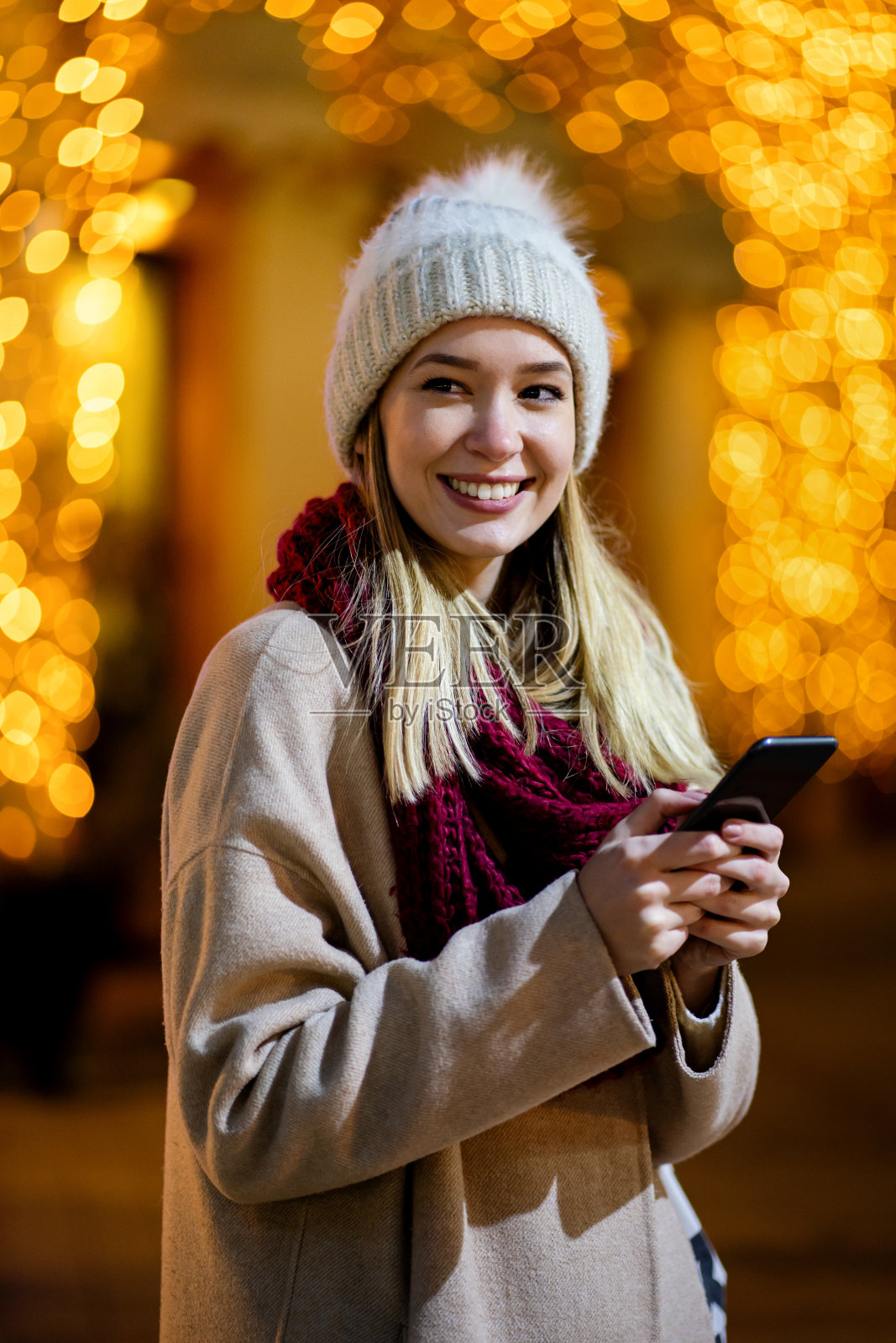 快乐的美丽女子女孩使用智能手机在城市与喜庆的圣诞集市背景照片摄影图片