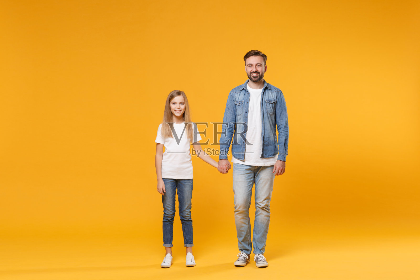 微笑的大胡子男人穿着便服和小女孩玩得很开心。父亲小女儿孤立在黄色背景的工作室肖像。爱家庭，亲子，童年观念。手牵手。照片摄影图片