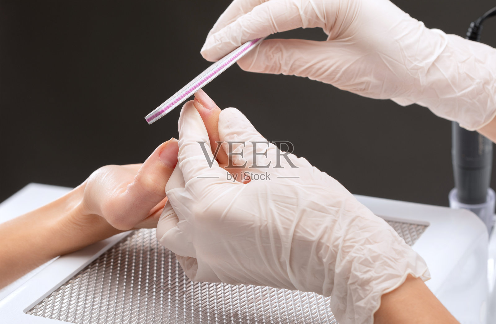 美甲大师在美容院的指甲延伸过程中锯附一个指甲形状。专业的双手护理。照片摄影图片