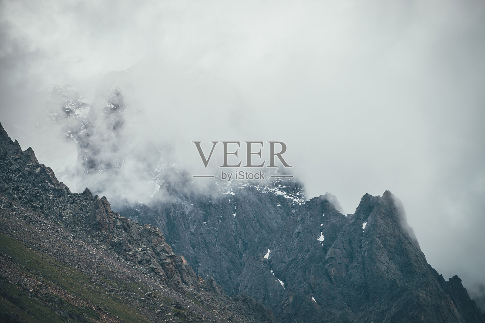 黑暗的大气超现实景观与黑暗的岩石山顶在低云在灰色多云的天空。灰色的低云在高高的顶峰。高高的黑色岩石，低低的云里有雪。超现实主义的山脉。照片摄影图片