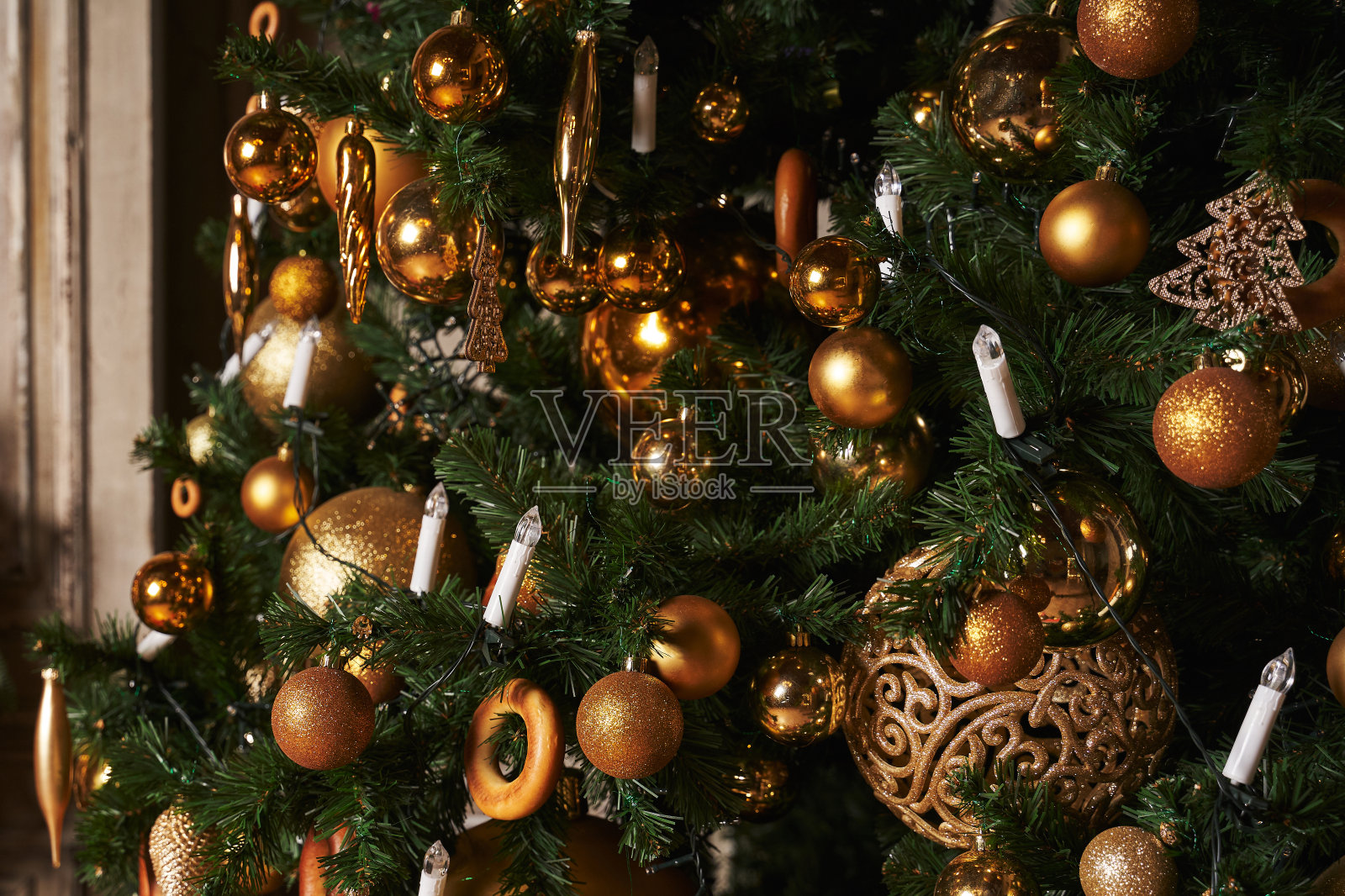 圣诞树上有金球和其他玩具。蜡烛形状的花环照片摄影图片