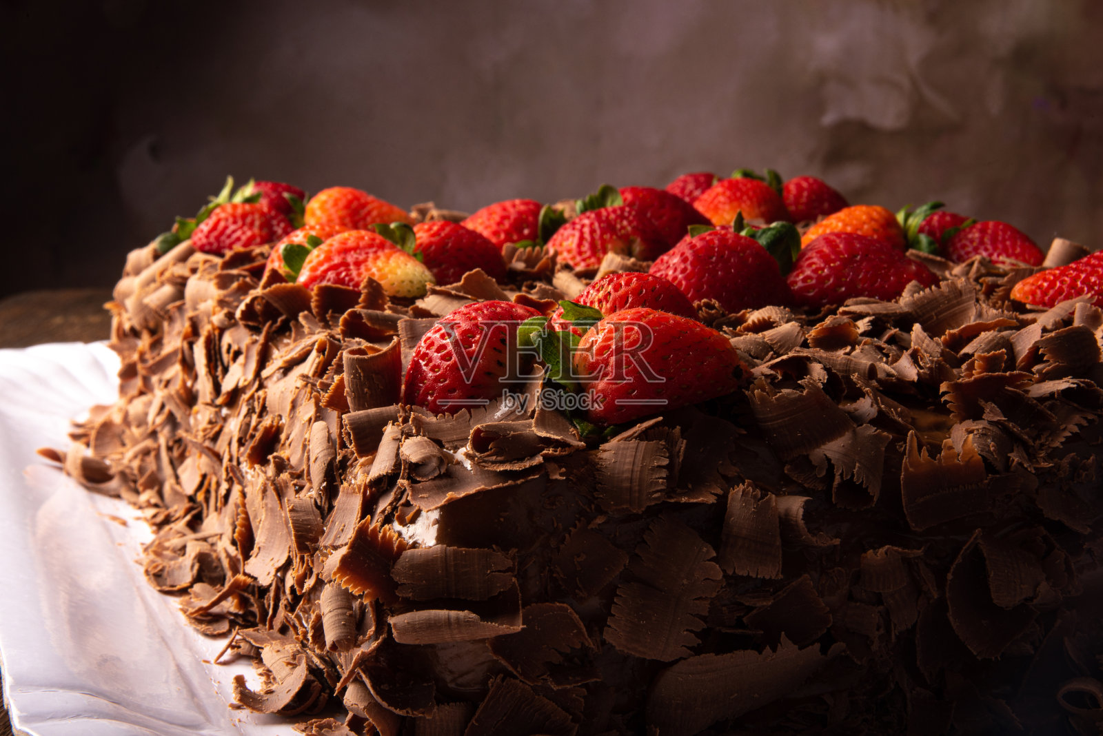 巧克力蛋糕，一个美丽的巧克力蛋糕草莓上的白色形状的乡村木材，抽象的背景，选择性的焦点。照片摄影图片