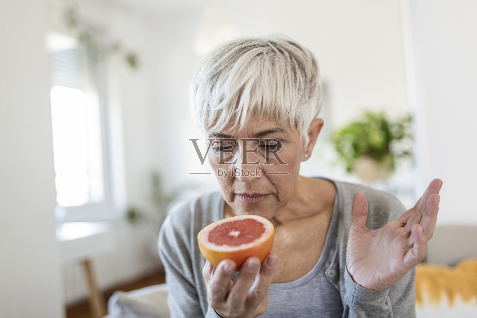 生病的女人试图感觉一半新鲜橙子的气味，有Covid-19，冠状病毒感染的症状-丧失嗅觉和味觉。这种疾病的主要症状之一照片摄影图片