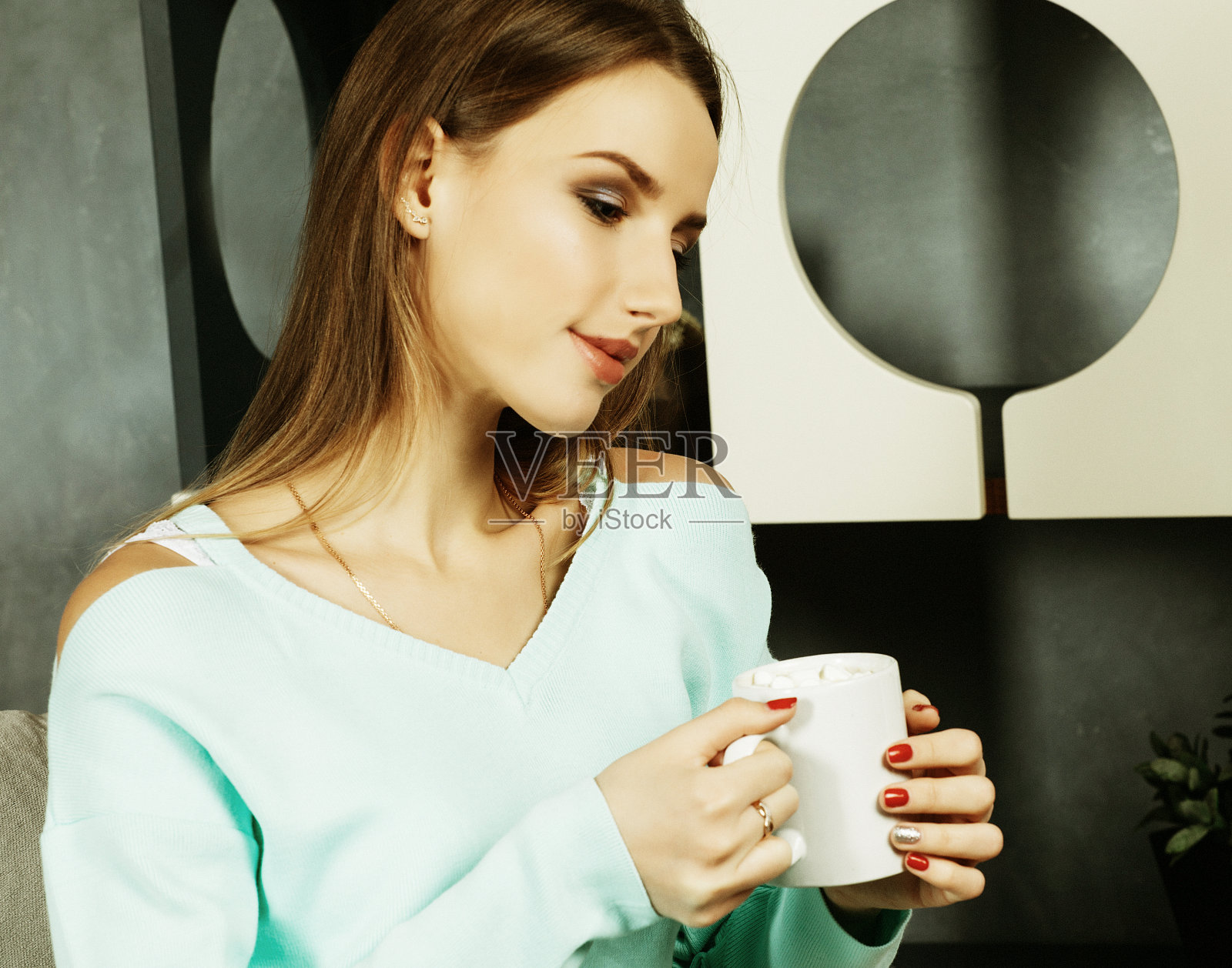 美丽和可爱。漂亮的年轻女子拿着咖啡杯，坐在家里的椅子上。生活方式的概念照片摄影图片