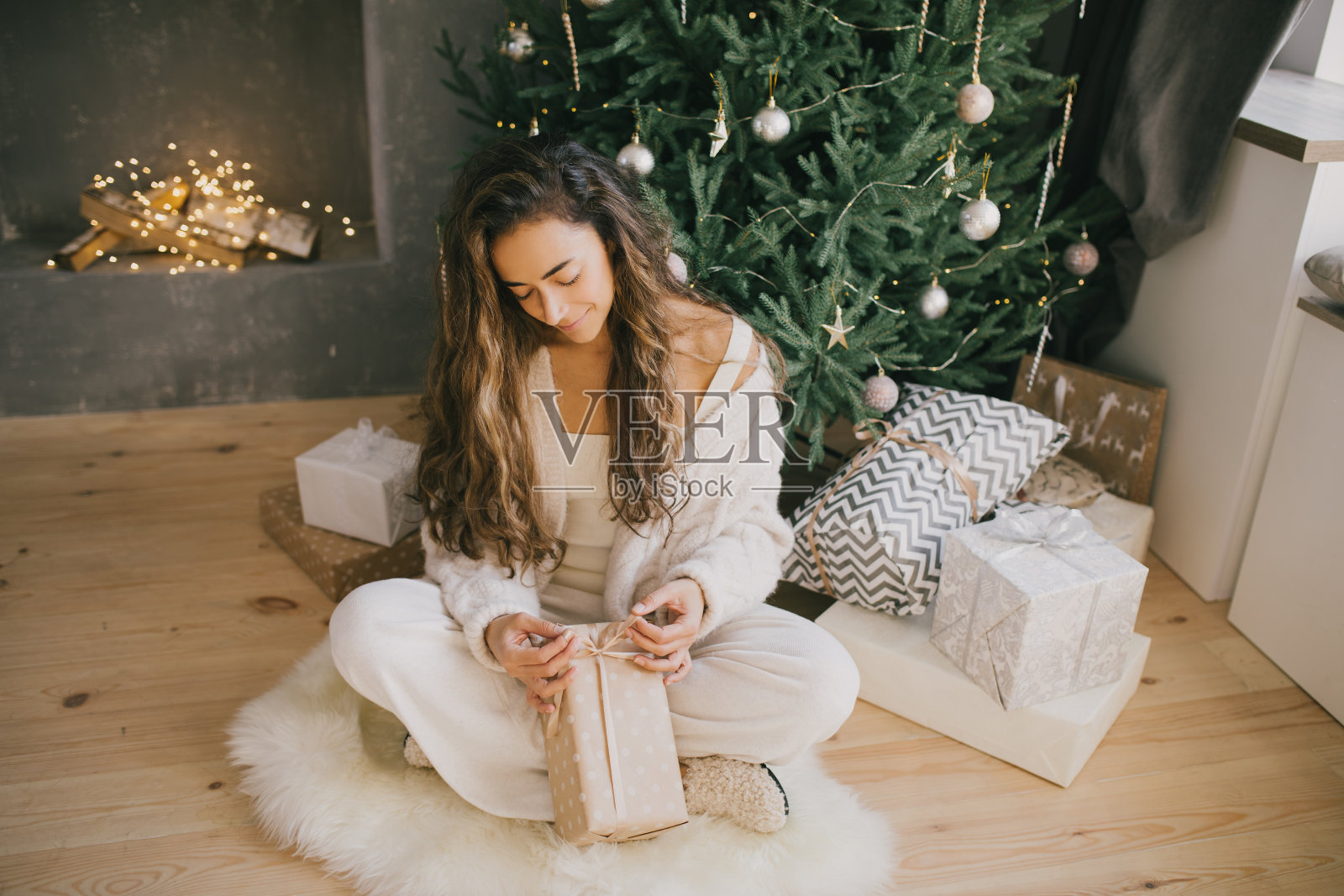 年轻漂亮的女人拿着礼品盒在一间舒适的房间里，背景是圣诞树和礼物。照片摄影图片
