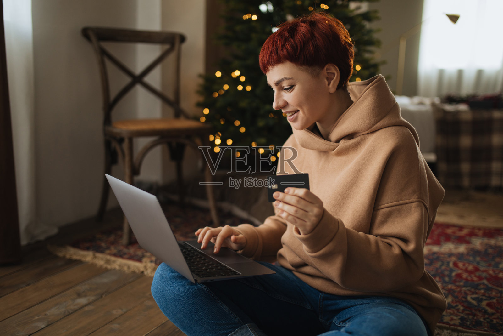 一名年轻女子在舒适的房间里用信用卡坐在笔记本电脑前网购圣诞礼物。照片摄影图片