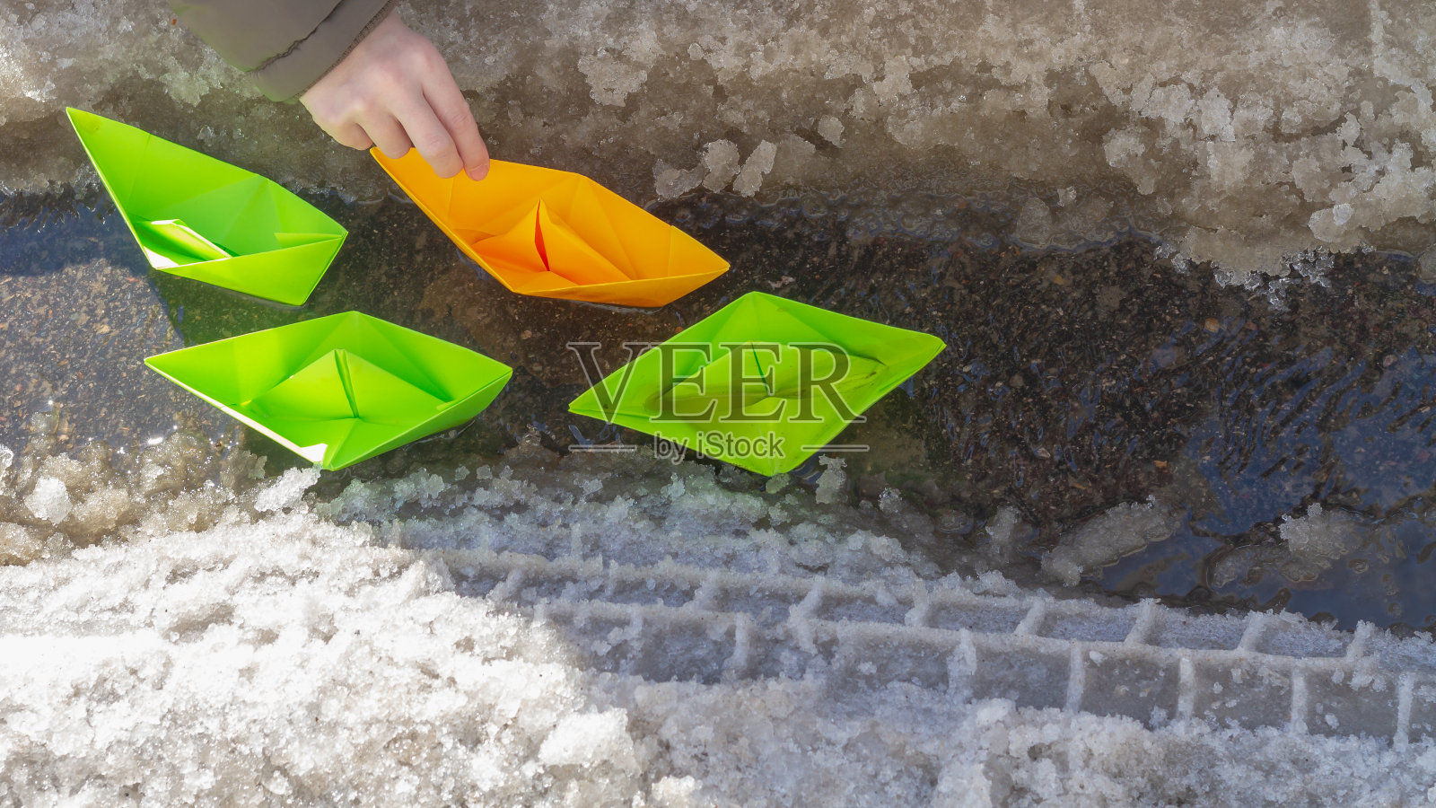 春天的路上，绿色和橙色的纸船漂浮在小溪上照片摄影图片