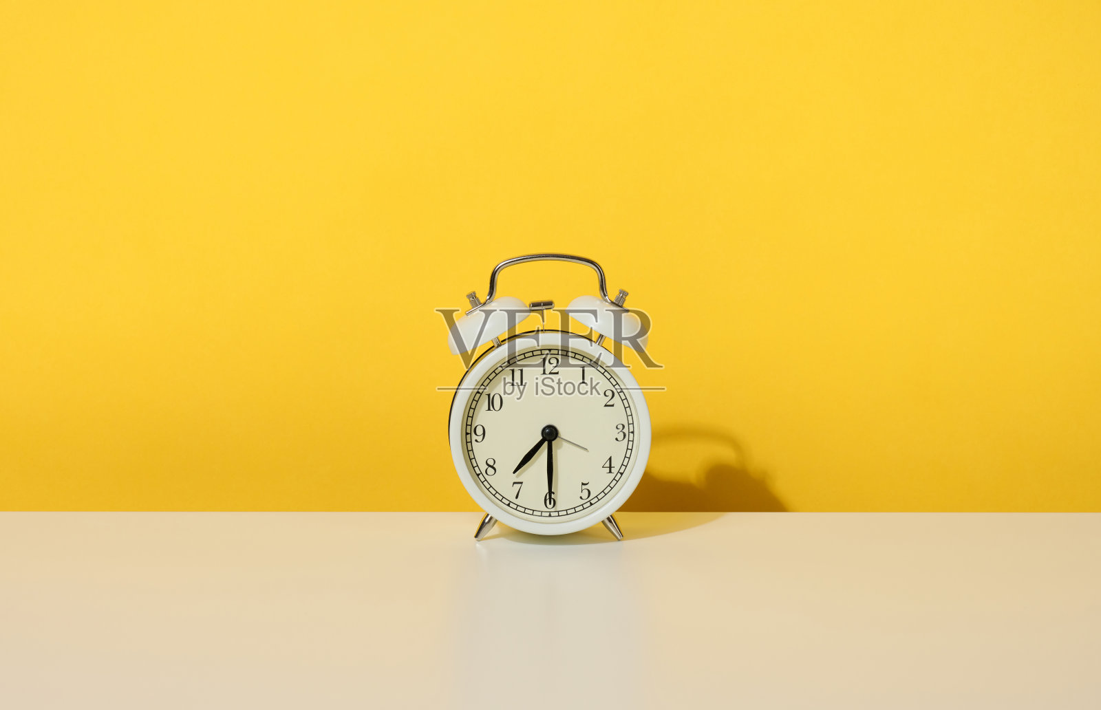早上七点半，白色的桌子上放着一个圆形的闹钟。黄色背景照片摄影图片