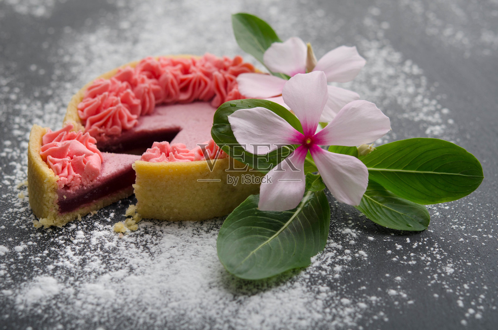 奶油蛋糕上装饰着白色的花和绿色的叶子，在黑色的表面上撒着糖粉。照片摄影图片