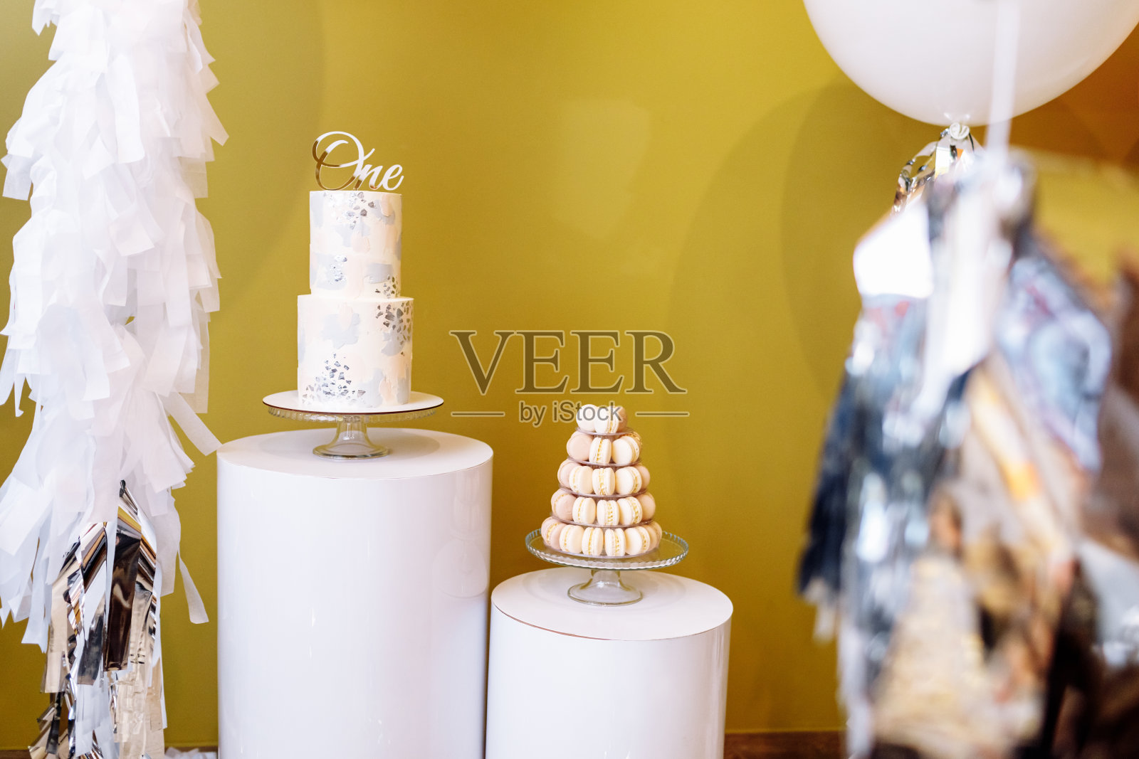 用两个故事蛋糕和大的白色和米色气球装饰一岁生日。带有马卡龙或马卡龙的糖果条。生日聚会。有选择性的重点照片摄影图片