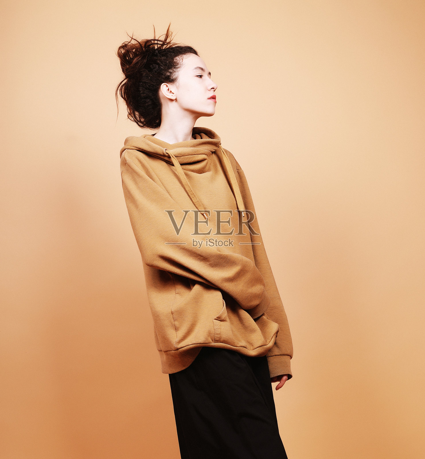 年轻的褐发模特在工作室摆姿势，米色背景照片摄影图片