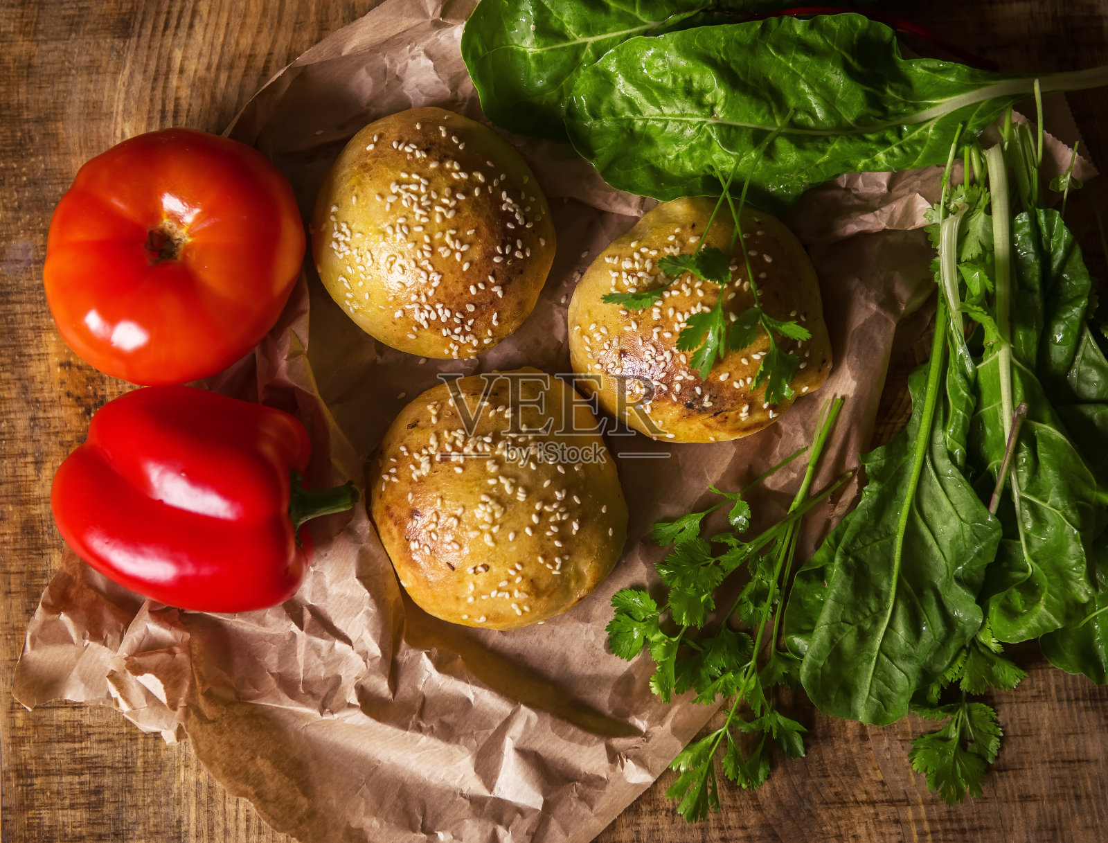 新鲜自制的芝麻汉堡包，放在手工烘焙纸上，和蔬菜放在一起。制作素食汉堡的材料。烹饪博客,菜谱。有选择性的重点。开胃的照片摄影图片