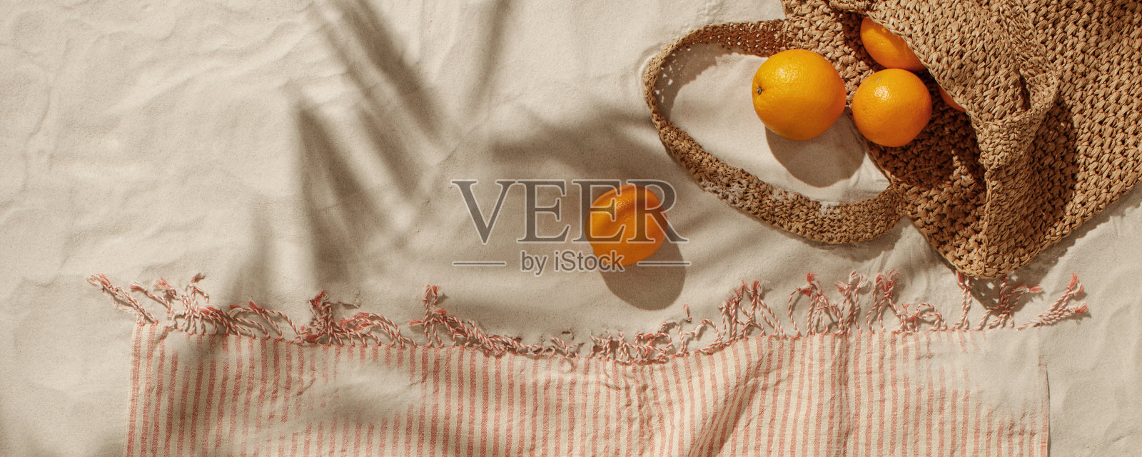 新鲜的橙子从编织袋里掉在沙滩上。带有流苏细节的亚麻沙滩毛巾。热带度假概念照片摄影图片