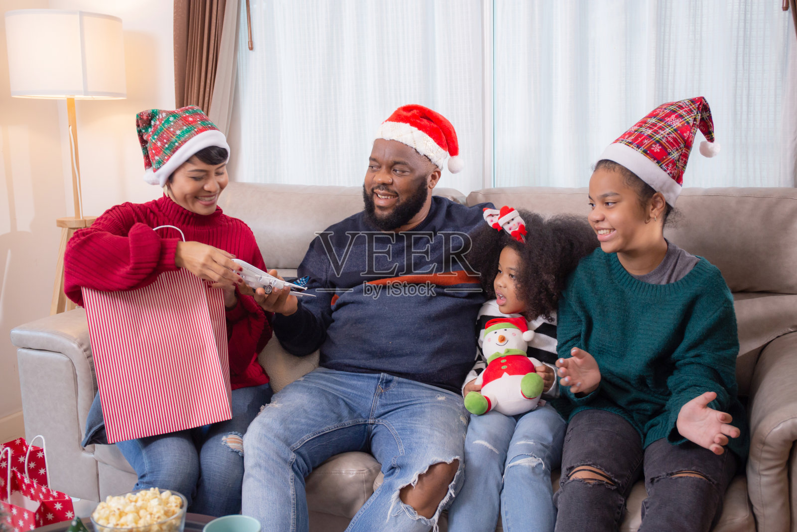 快乐的非洲家庭妈妈给一个购物袋的礼物庆祝与爸爸和女儿在家里的客厅为惊喜在平安夜的一天，新的紫杉，节日和节日。照片摄影图片