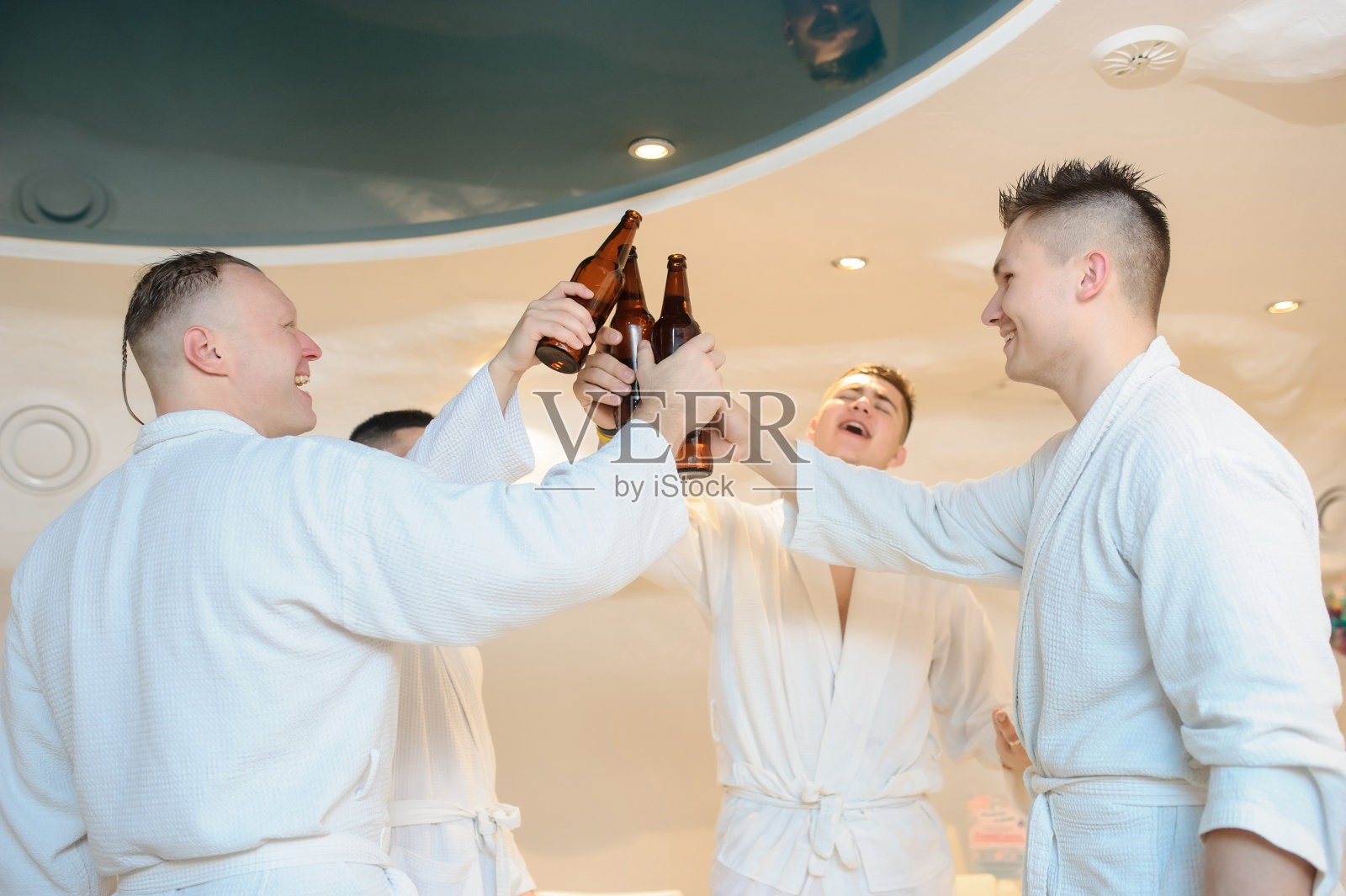 身穿白大褂的男子在蒸桑拿后围坐在桌子旁，喝着啤酒照片摄影图片