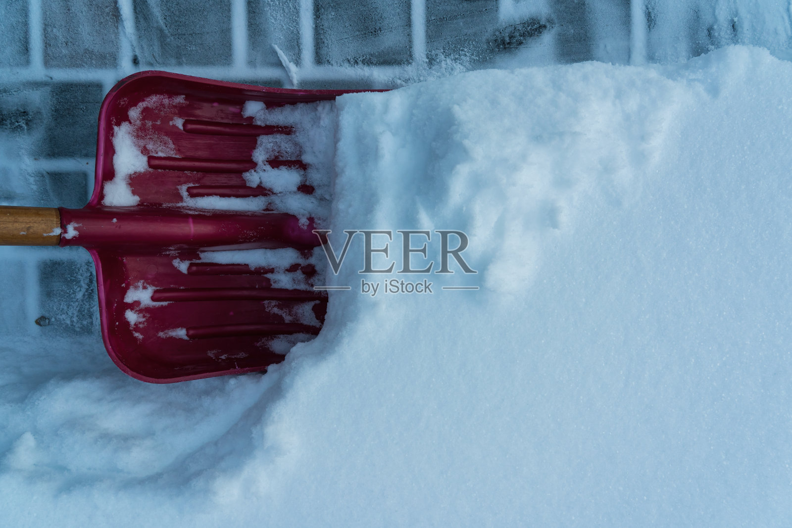 一把宽阔的红色铲子从水泥铺路板上刷下一层厚厚的新雪。背景。纹理。照片摄影图片