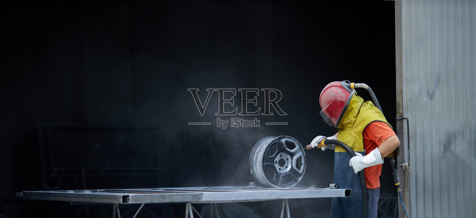 工作时使用喷砂机清理金属零件的男子照片摄影图片