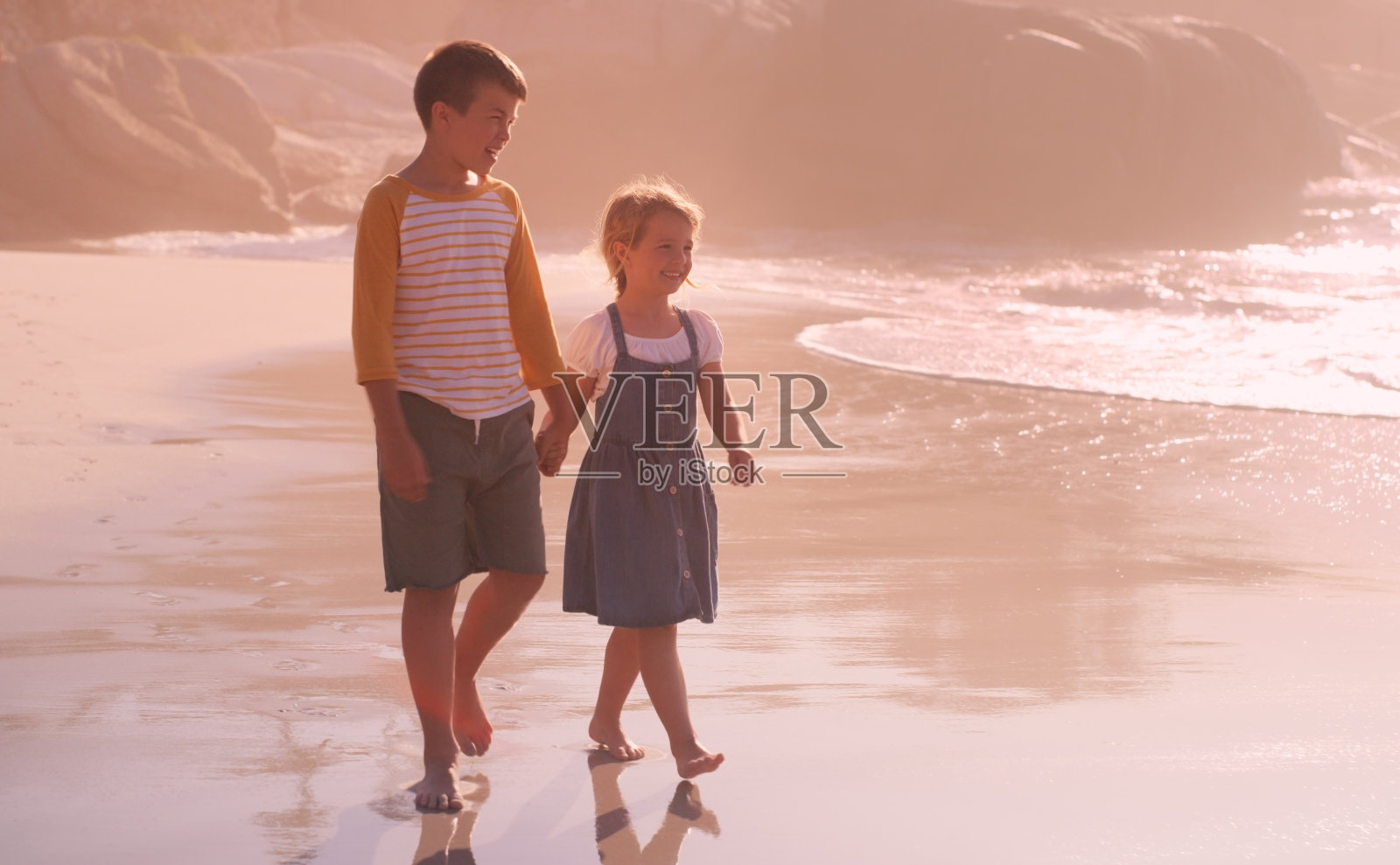一个可爱的小女孩和她哥哥手拉手在海滩上散步的全长照片照片摄影图片