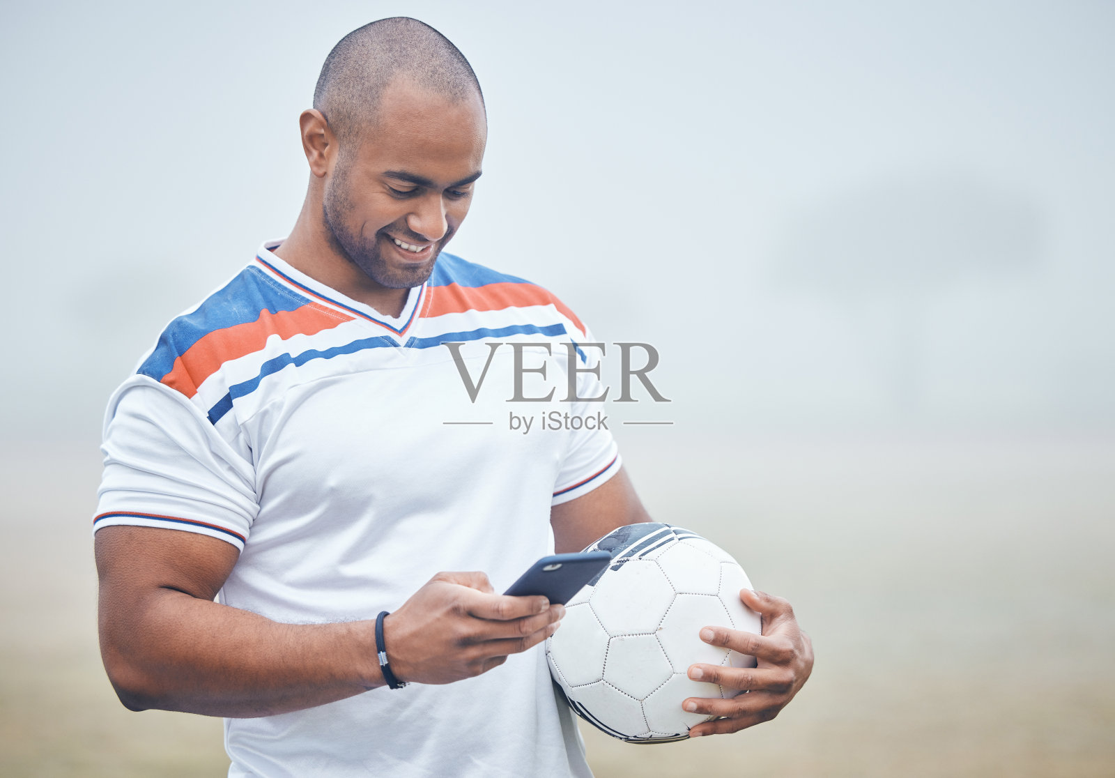 一名年轻男子足球运动员拿着球用智能手机发短信照片摄影图片