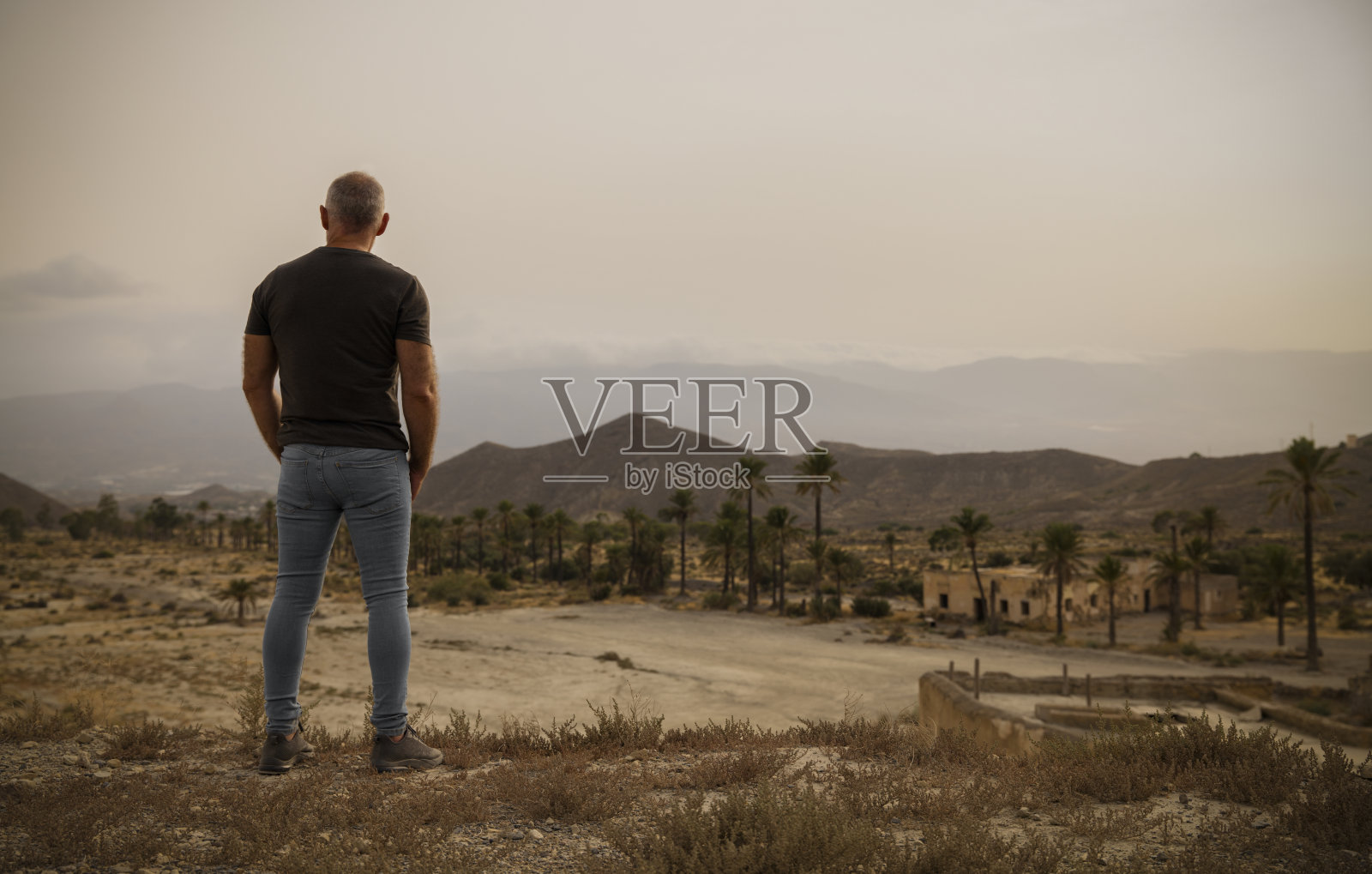 西班牙阿尔梅里亚塔伯纳斯沙漠的一名成年男子，在夏天带着一个被遗弃的村庄照片摄影图片