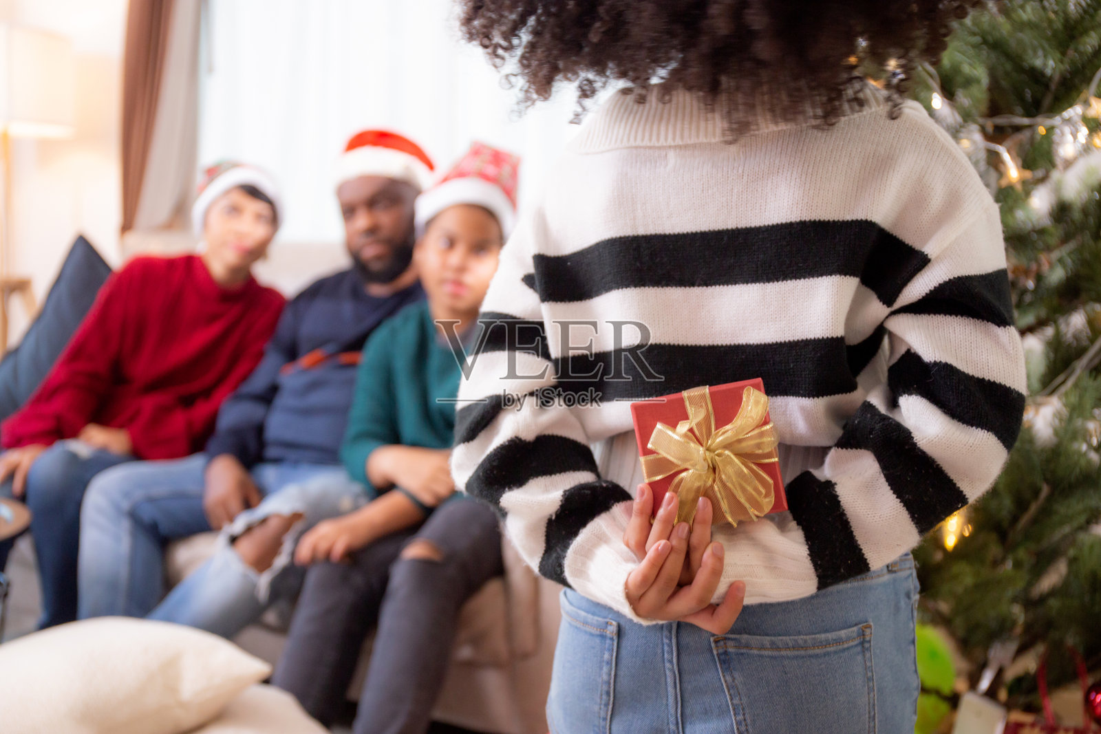 幸福非洲家庭带着女儿藏着礼物盒与爸爸妈妈在圣诞节当天在家里的客厅里，庆祝圣诞节、新年，孩子们与父母赠送礼物。照片摄影图片
