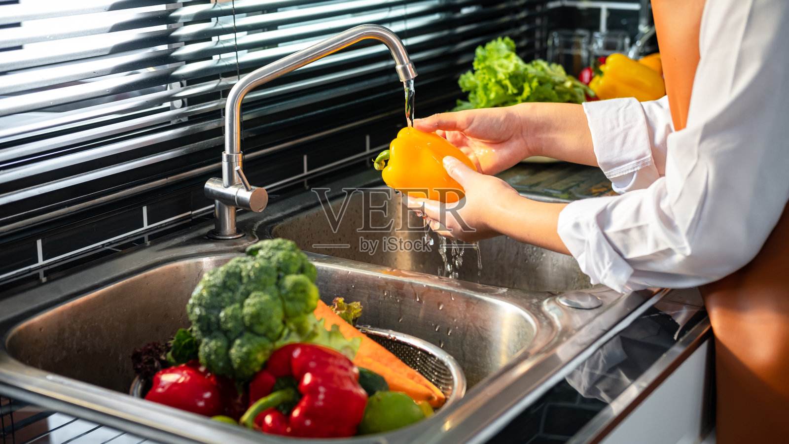 亚洲家庭主妇穿着围裙在水池里用滤菜器用水清洗花椒照片摄影图片