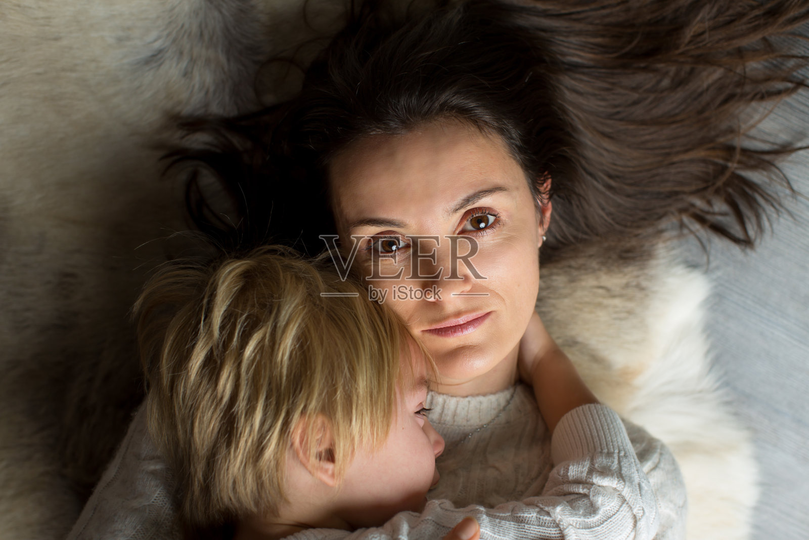 年轻的母亲，抱着啼哭的婴儿，躺在地板上拥抱照片摄影图片