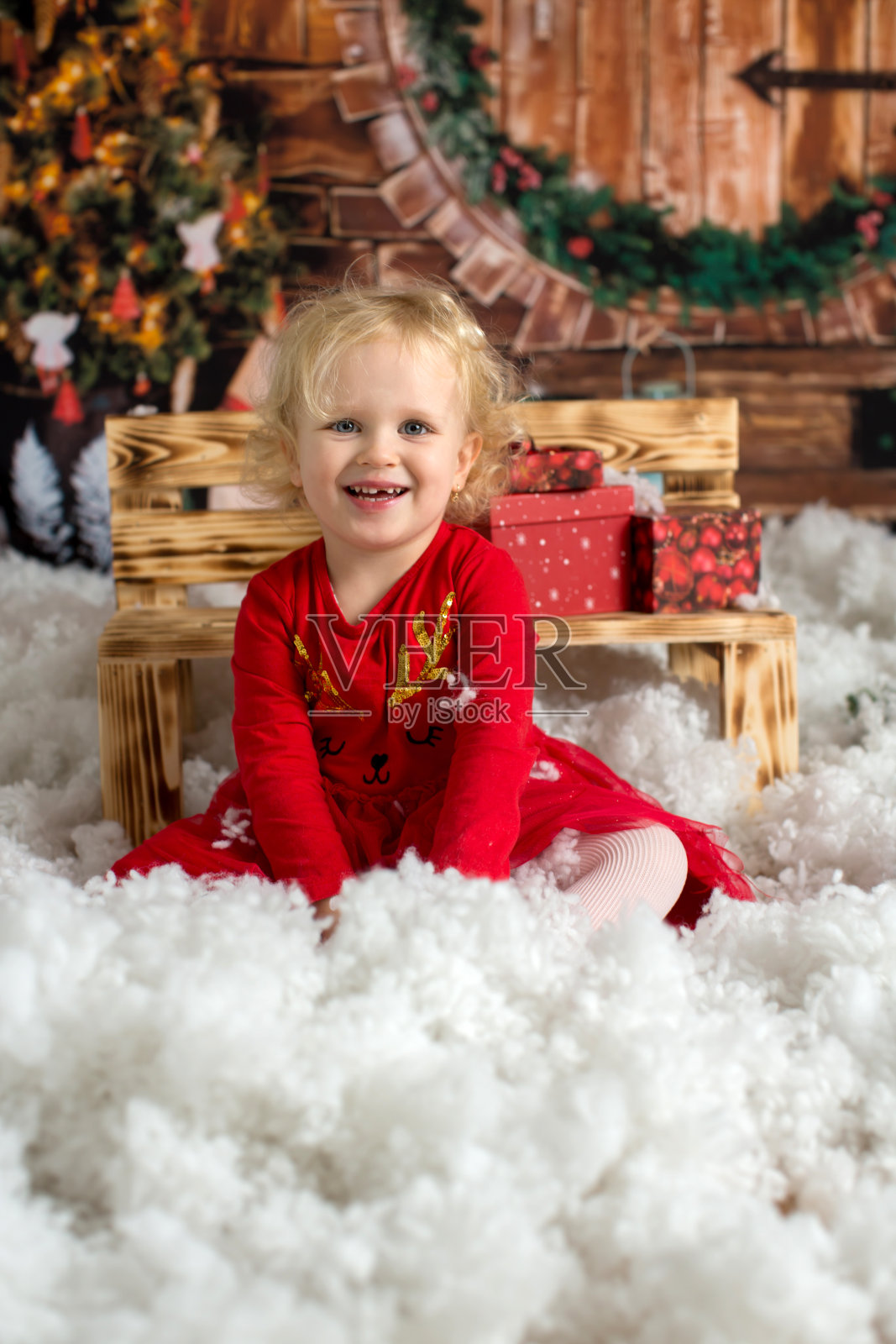 可爱的金发小女孩，卷发女孩，坐在装饰着圣诞装饰的木屋里，打开礼物照片摄影图片