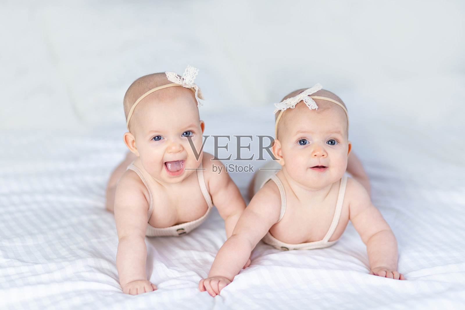 在家里白色的床上，两个穿着棉质套装的双胞胎女婴趴在床上笑着玩耍照片摄影图片