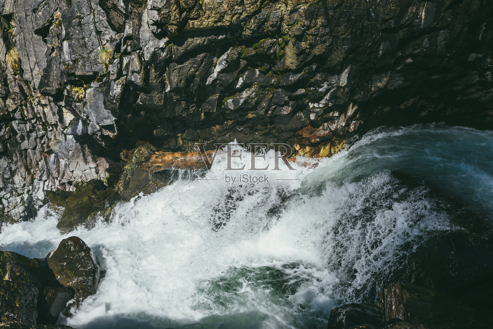 在阳光的照射下，在狭窄的峡谷中岩石间看到了绿松石般湍急的山河。大气山地景观与潮湿苔藓石在强大的山河流在阳光下。照片摄影图片