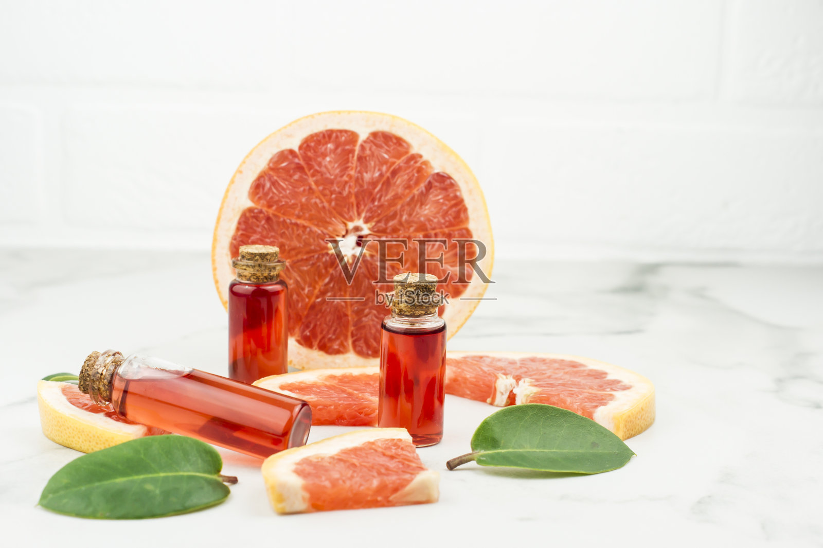 三个玻璃瓶，瓶塞上有油或葡萄柚精华，大理石背景上有水果泥。自然自我护理的终结。照片摄影图片