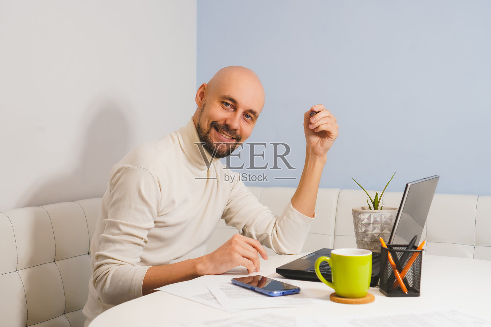 微笑的秃头男人胡子在白色高领衫工作在他的笔记本在家里，侧面看照片摄影图片