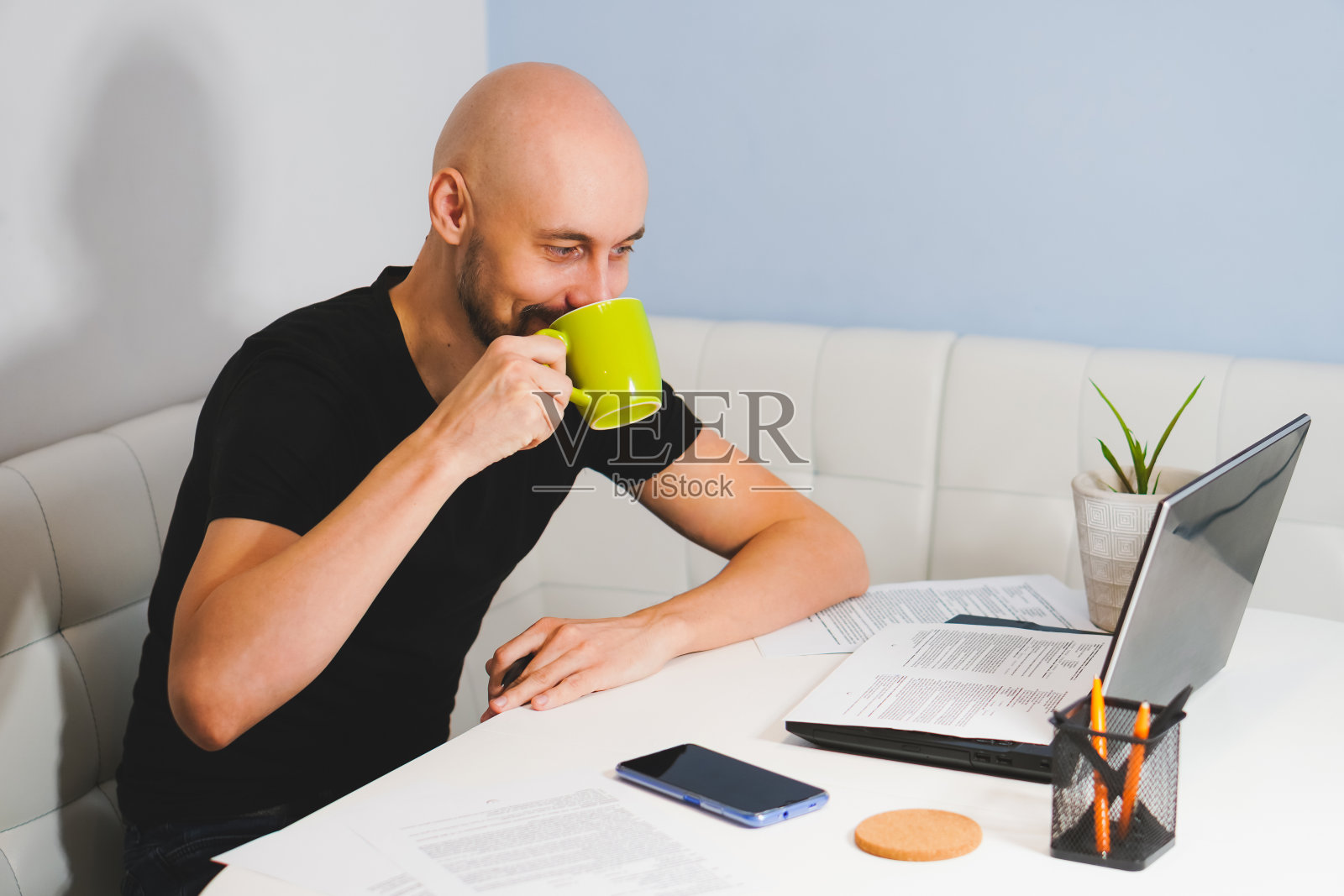 微笑的秃头男人胡子黑色t恤工作在他的笔记本在家里，侧面看照片摄影图片