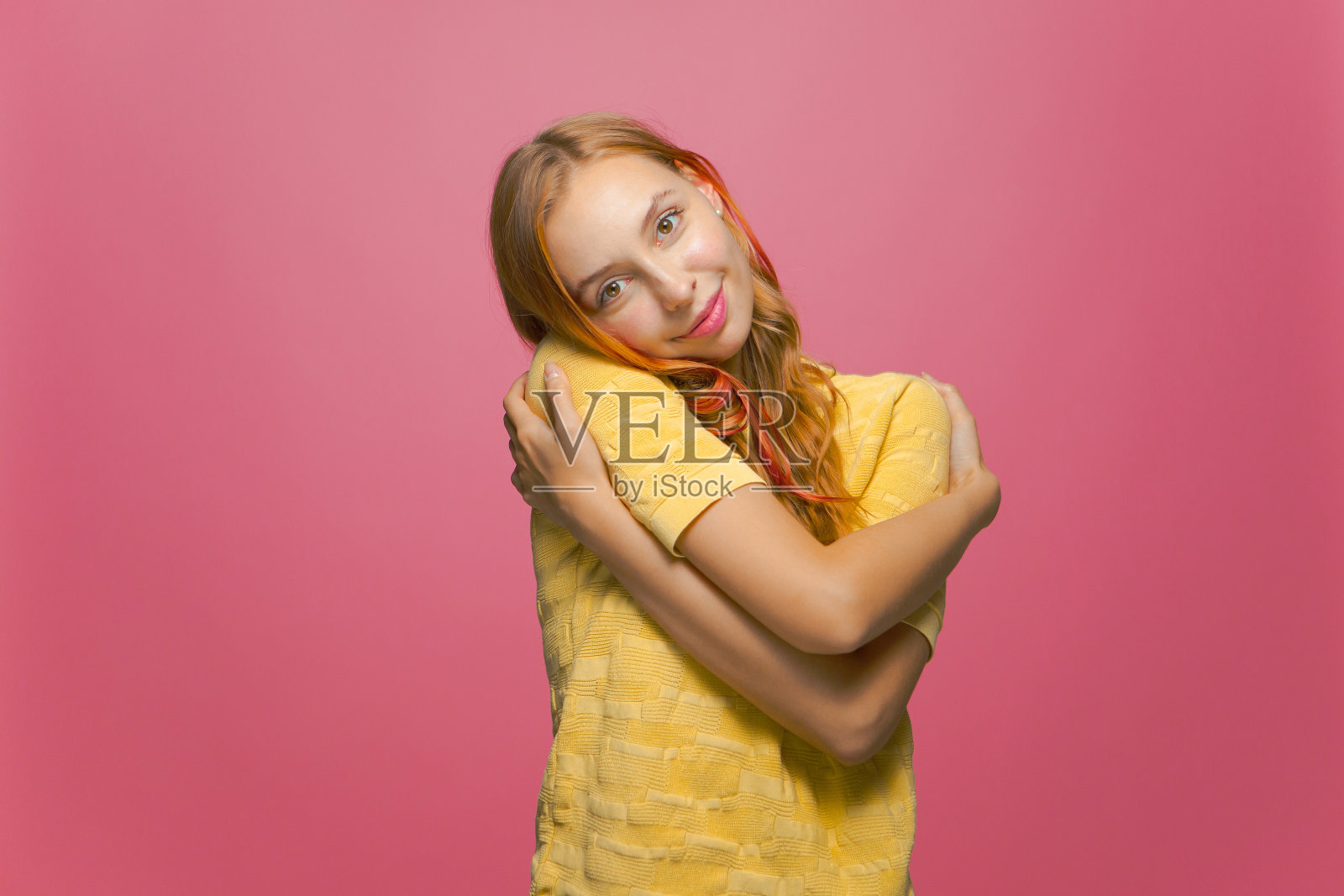 美丽的年轻女孩拥抱自己从快乐的粉红色背景微笑。自爱，积极自尊观念照片摄影图片